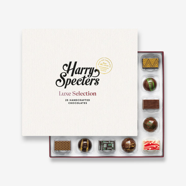 A box of 25 artisan chocolates by Harry Specters including Birthday themed designs partially covered by a box lid 