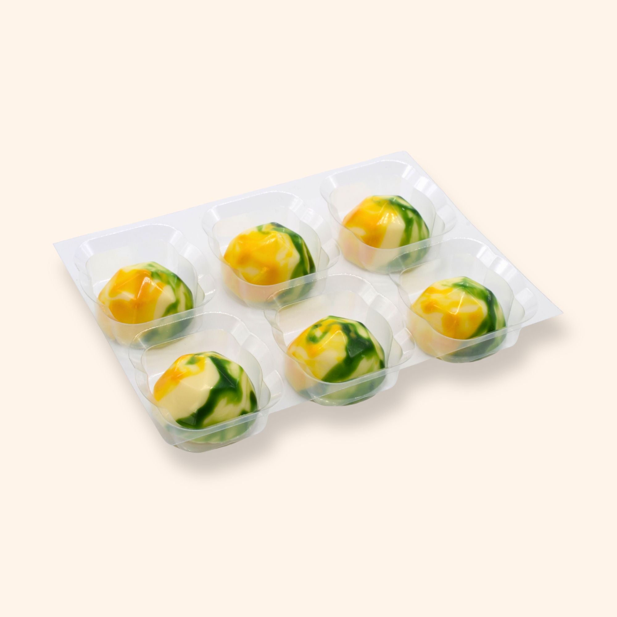 Lemon elderflower chocolates with green and yellow design in a clear tray on a light beige background