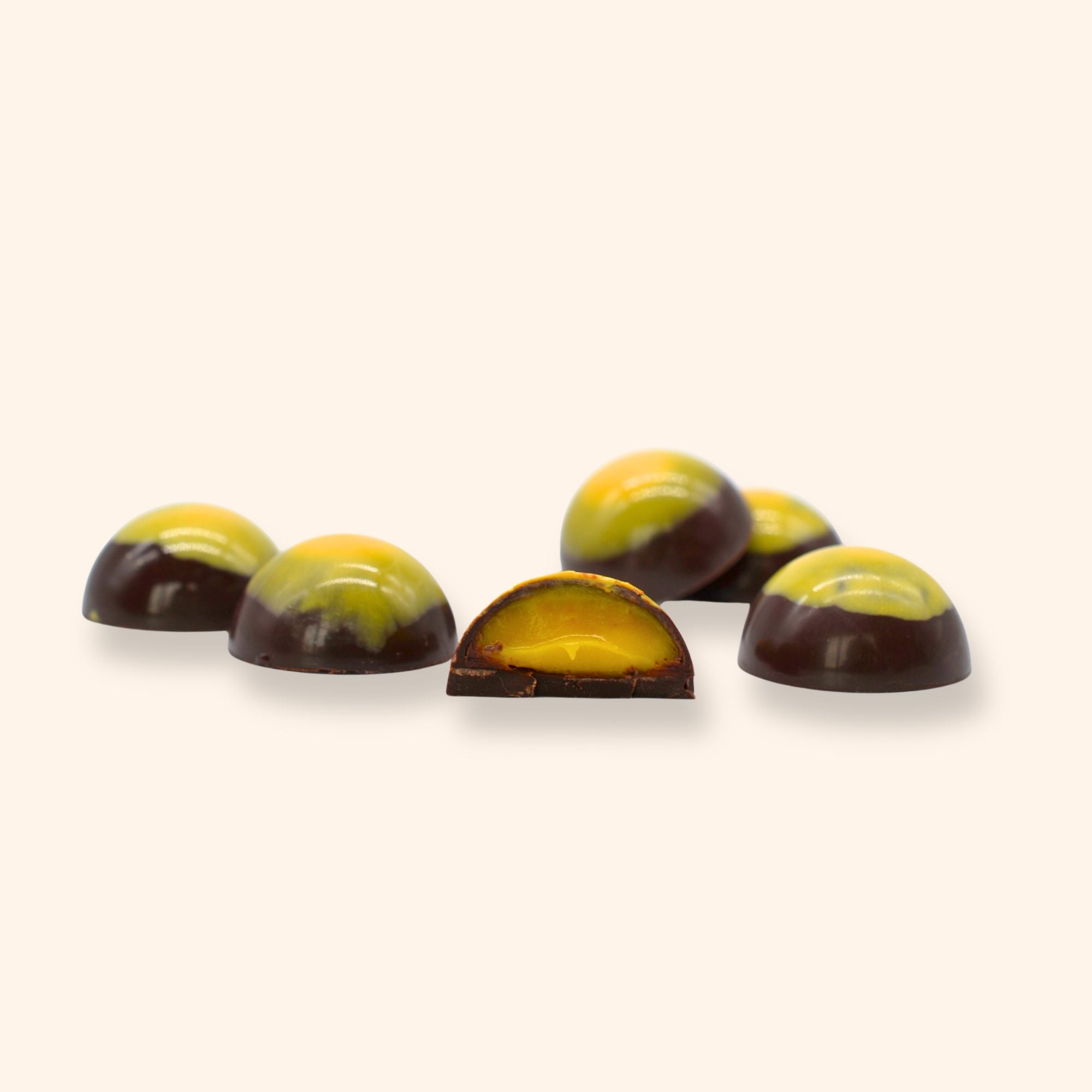 Six mango calamansi chocolates with one cut open revealing a creamy filling on a beige background