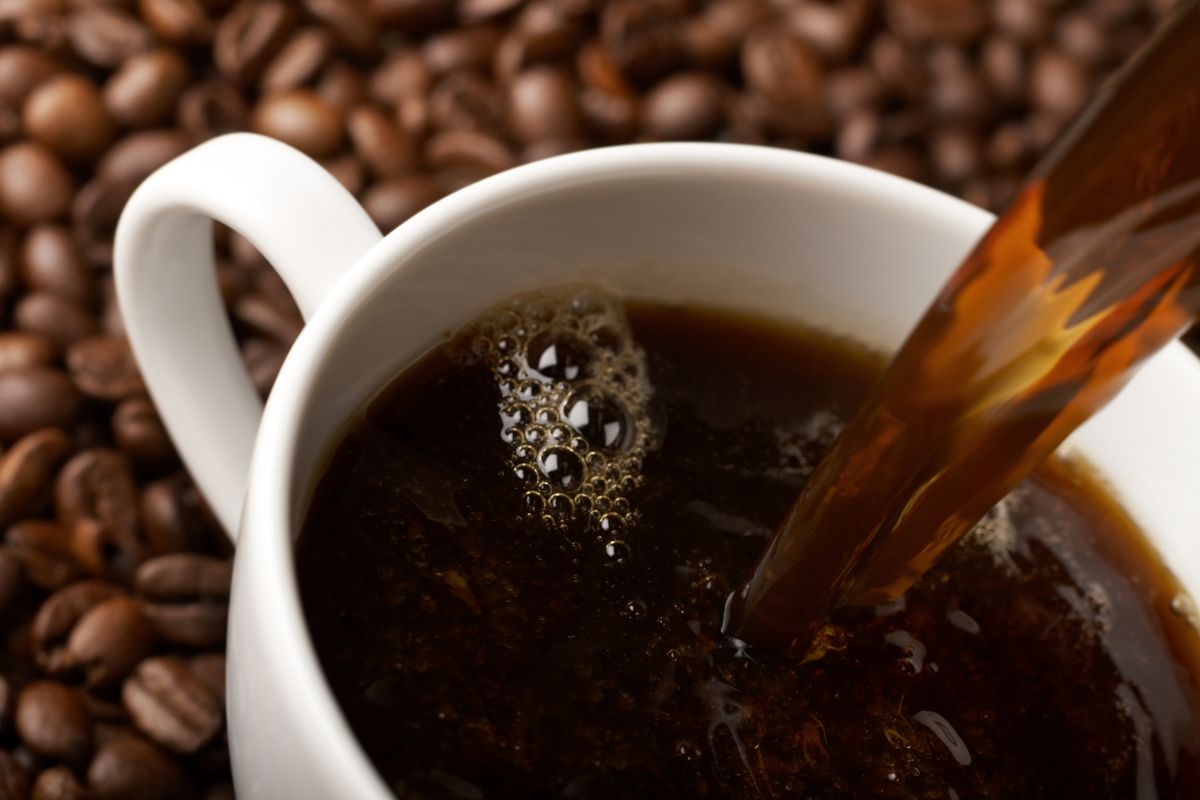 Hot coffee being poured into a cup which sits on a bed of coffee beans