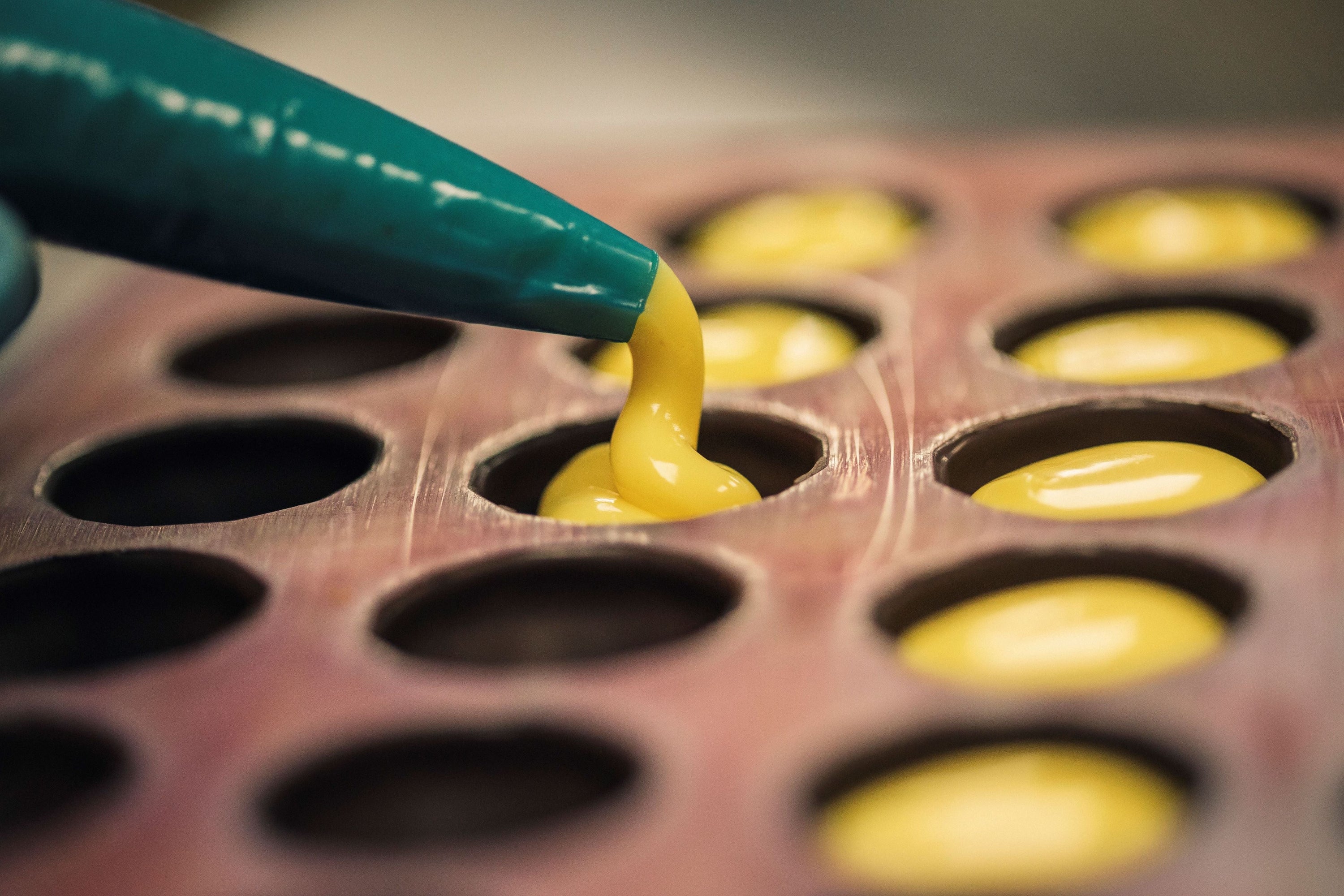 A rich yellow colour chocolate ganache being piped into a mould.