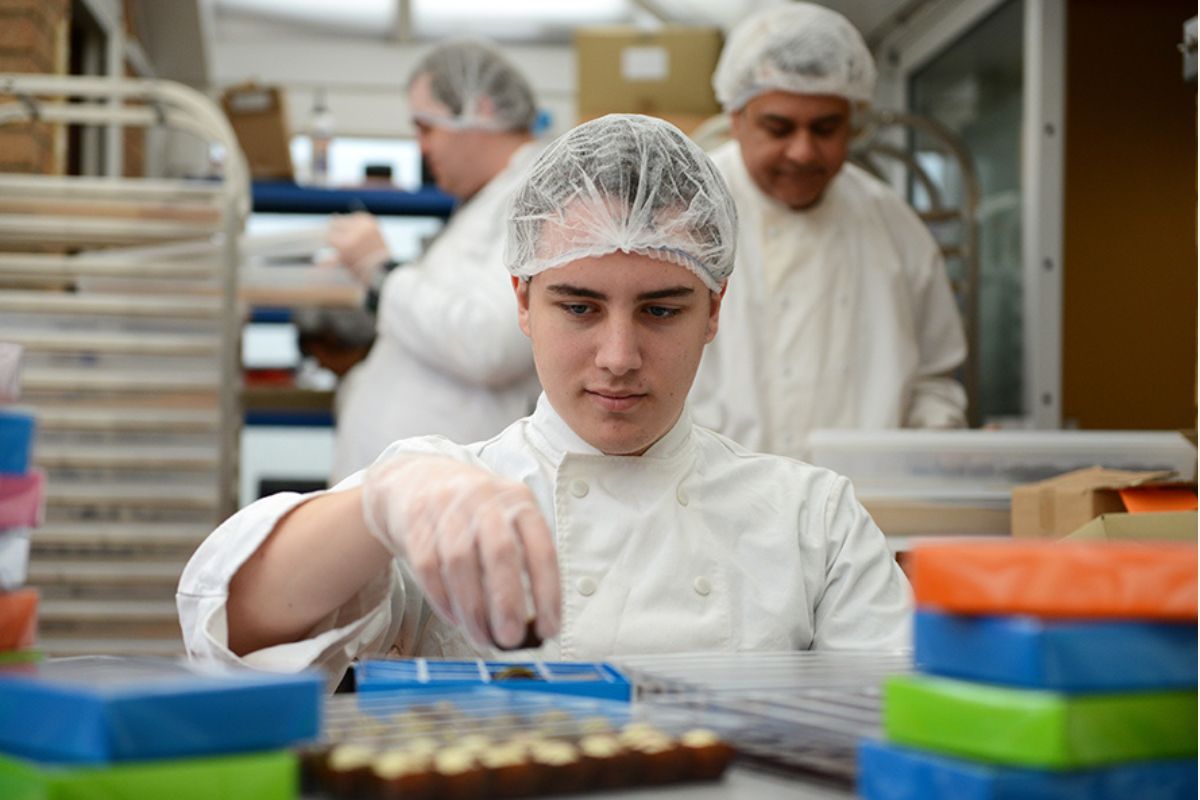 Person in a chocolate making facility wearing a hairnet and gloves.