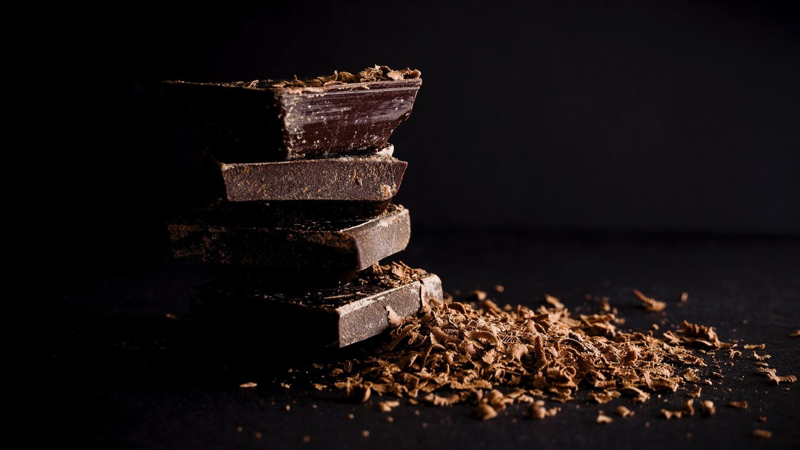 A stack of dark chocolate squares next to a pile of chocolate shavings