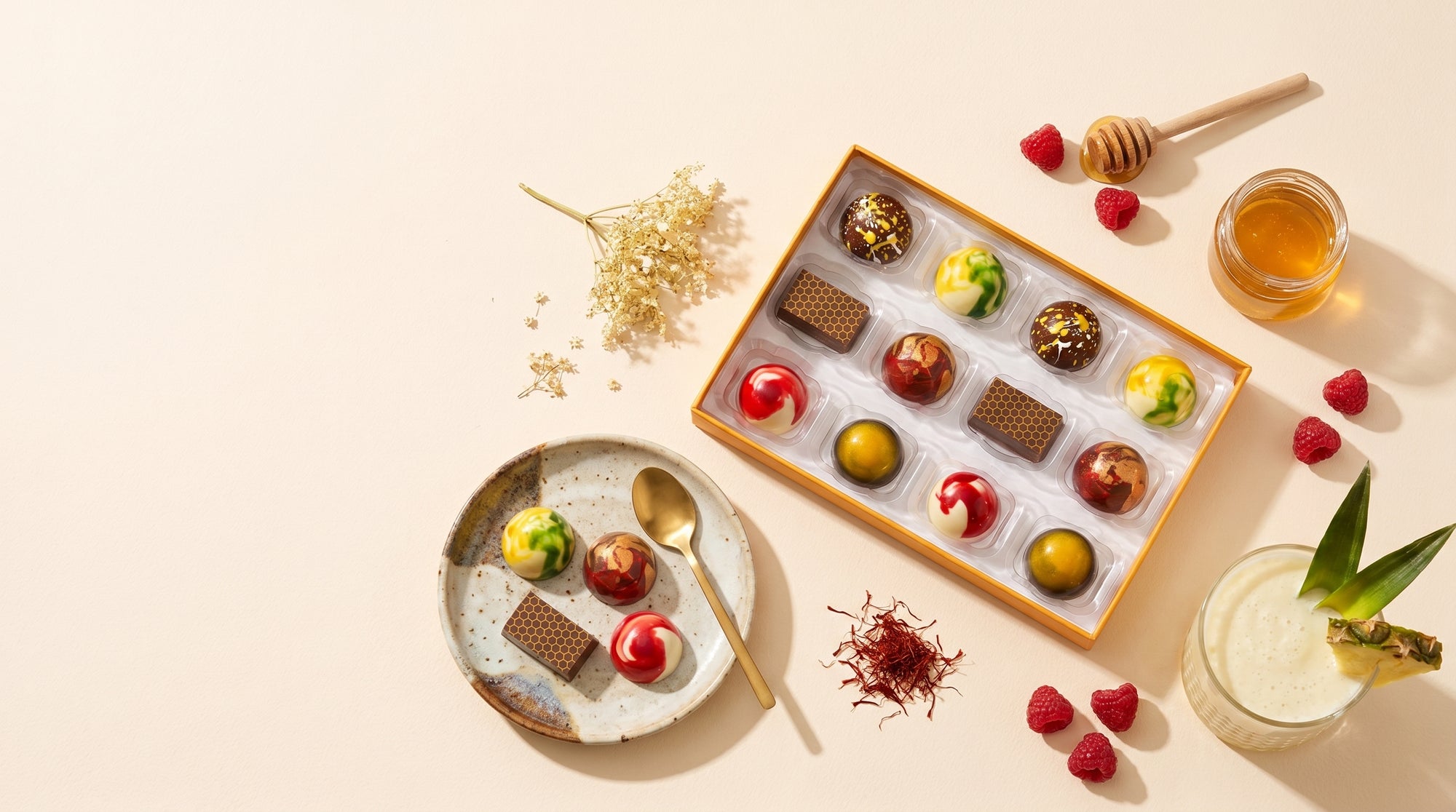 Assorted chocolates in a box with a plate of chocolates and a pina colada on a beige background