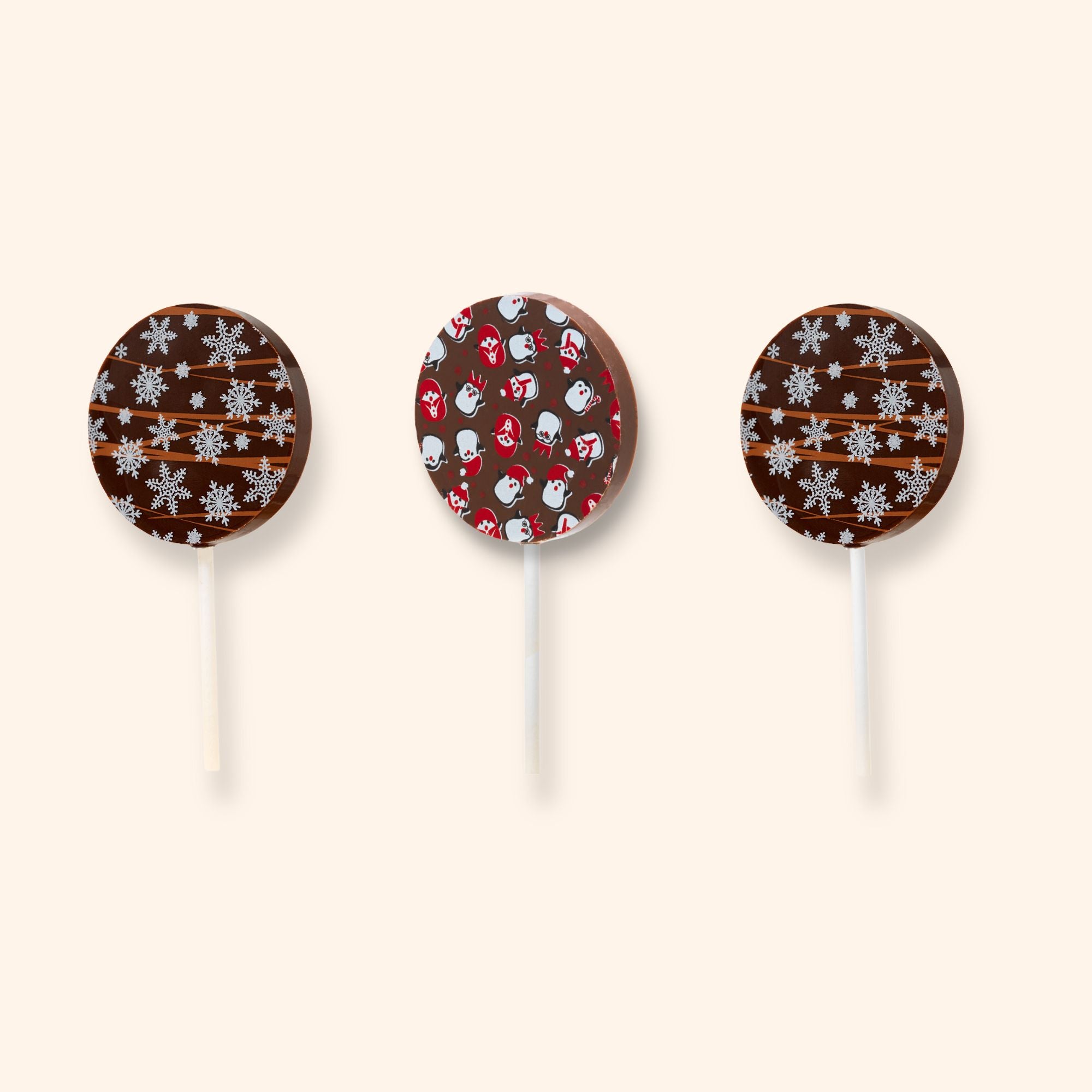 Three milk chocolate lollipops with Christmas patterns on a beige background
