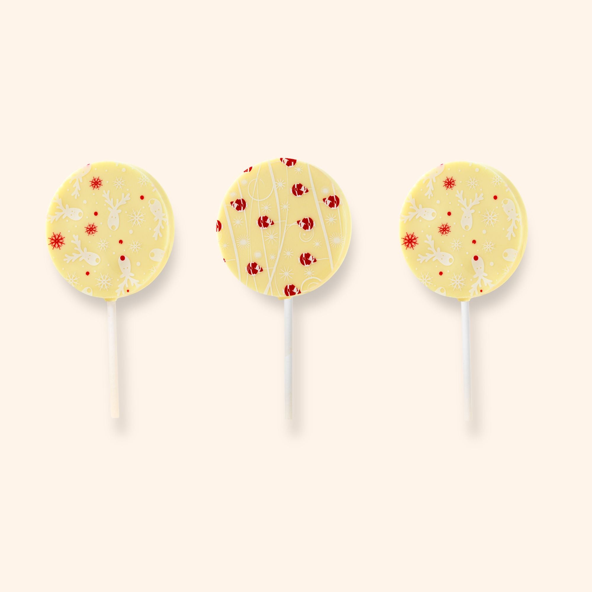 Three white chocolate lollipops with Christmas patterns on a beige background