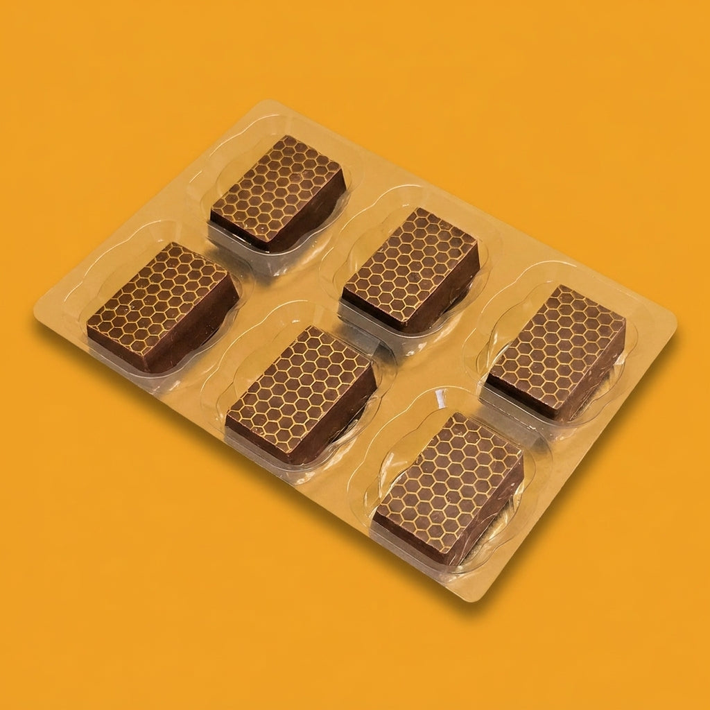 Six honey saffron milk chocolates in a tray, decorated with a honeycomb pattern on an orange background