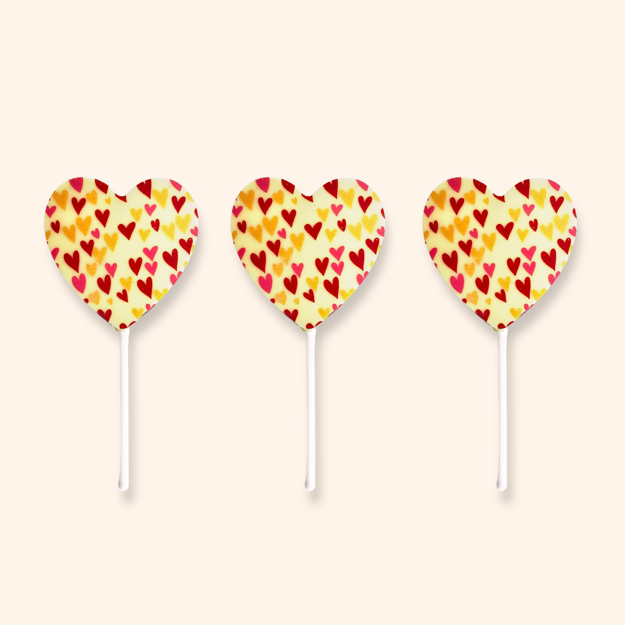 Three white chocolate heart-shaped lollipops with colourful heart patterns on a light beige background
