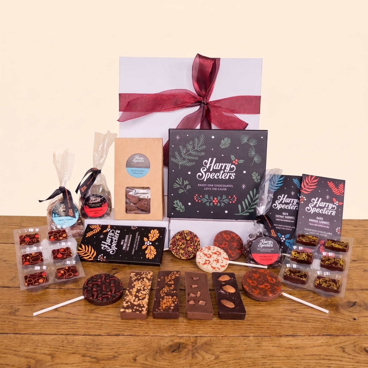 A chocolate gift hamper from Harry Specters arranged on a wooden table with a white and burgundy gift box behind it. The assortment includes chocolate bars, lollipops, chocolate shapes, and packaged chocolates.