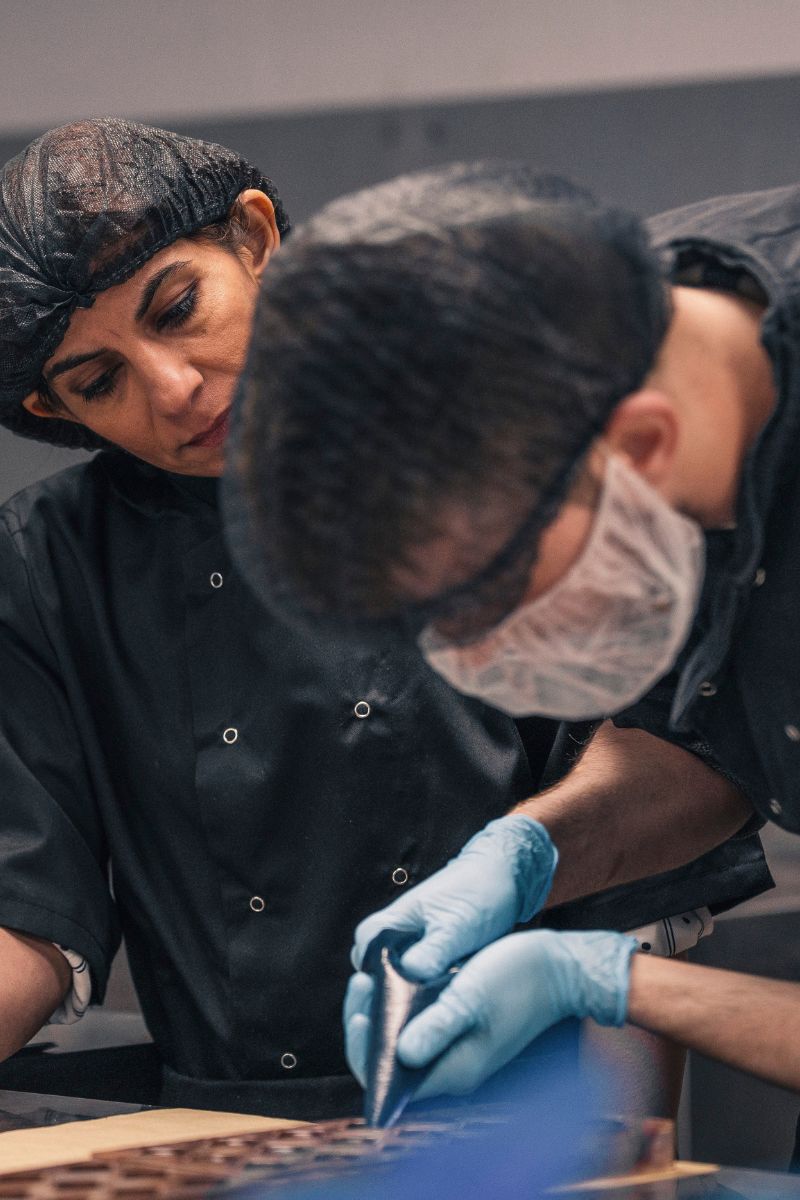 A autistic chocolatier in training, piping filling into chocolate moulds with supervision