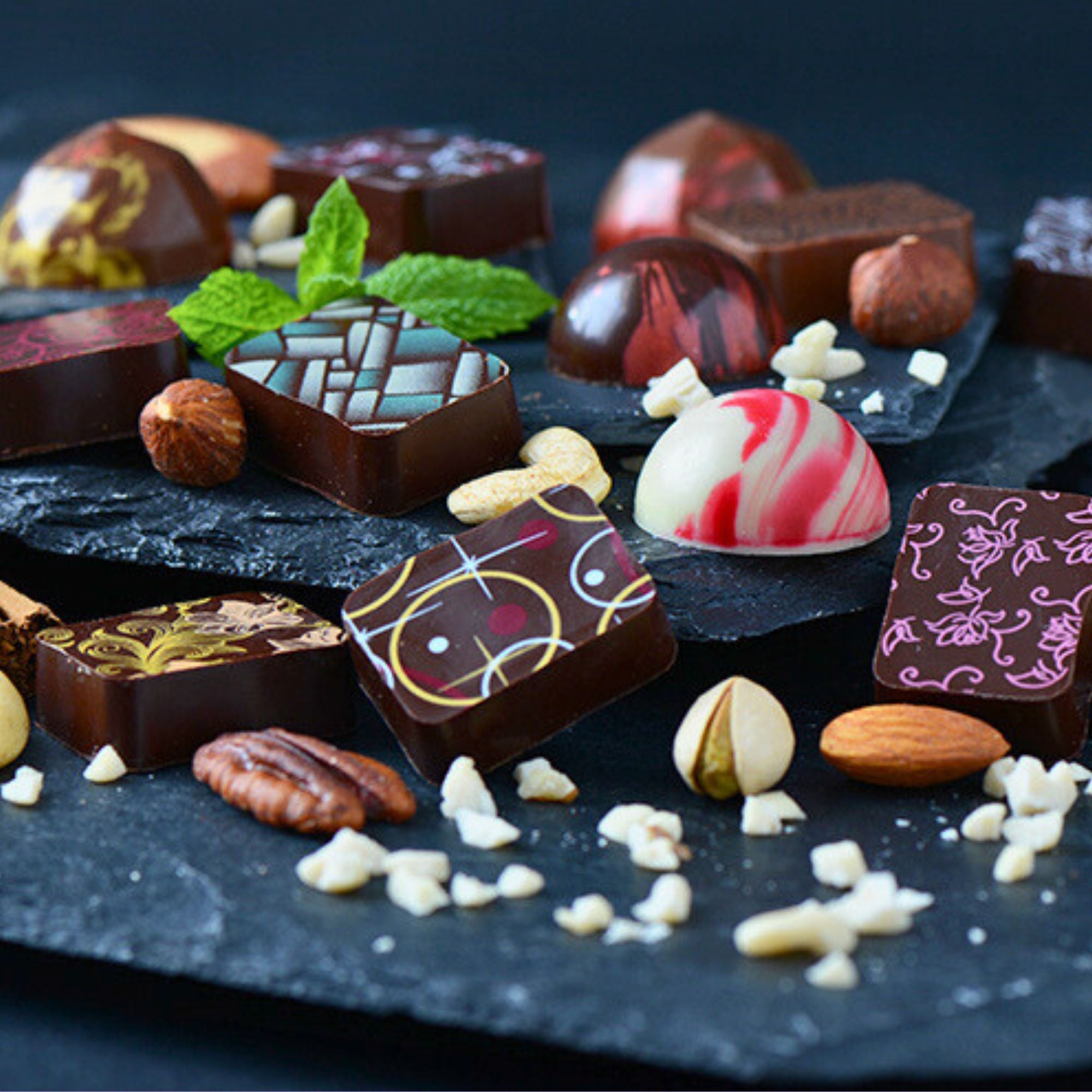 A selection of award-winning artisan chocolates on a slate background surrounded by fresh ingredients