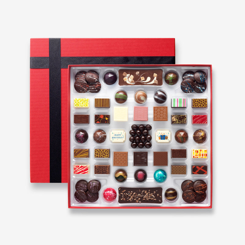 A chocolate box including buttons, bars, and coffee beans colourfully decorated and featuring two Birthday chocolates