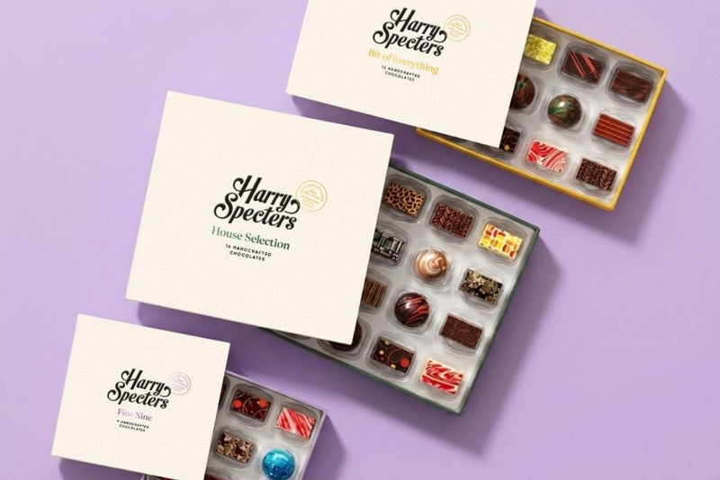 A chocolate subscription box on a yellow background, lid raised, twelve chocolates inside