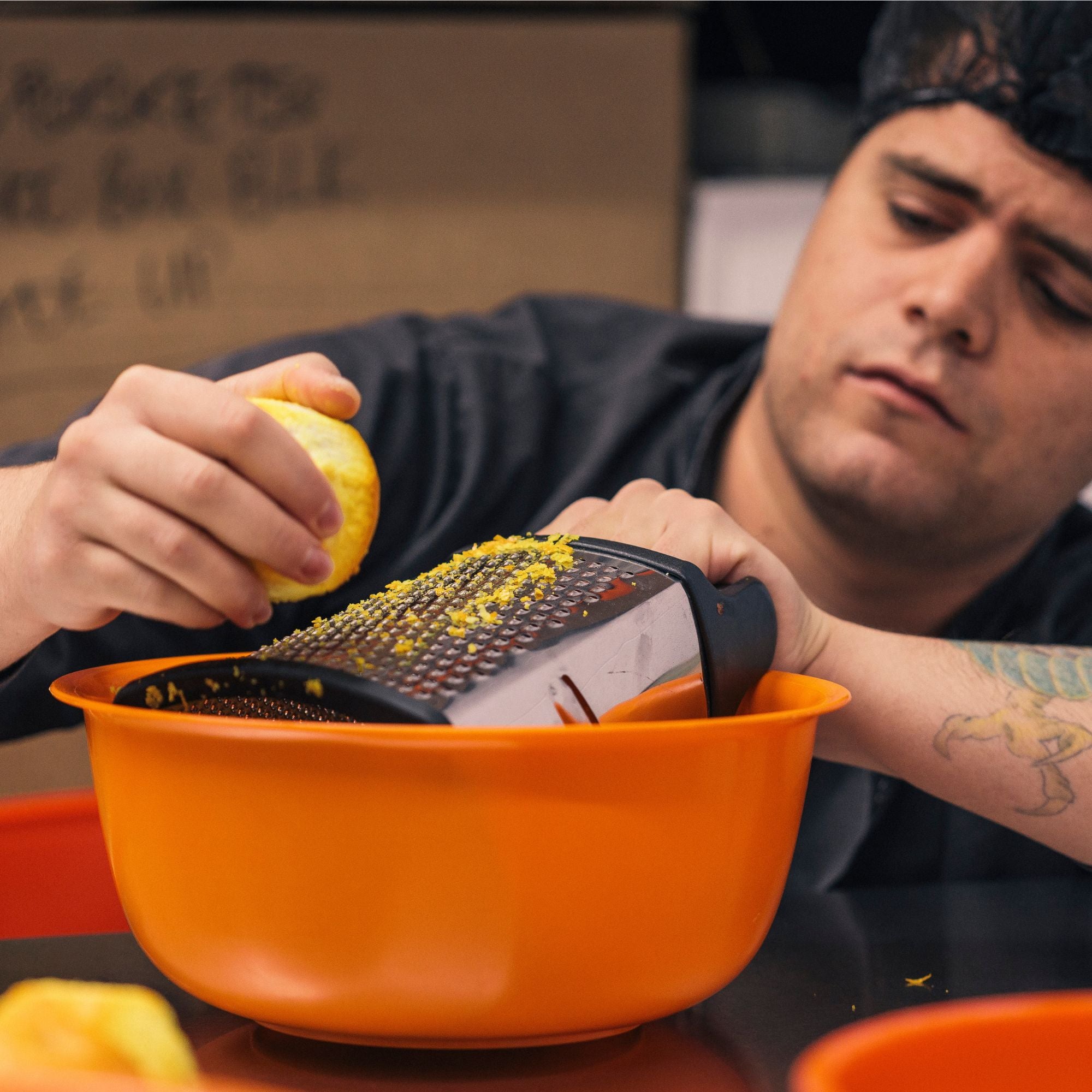 Person grating a lemon over an orange bowl with a box in the background
