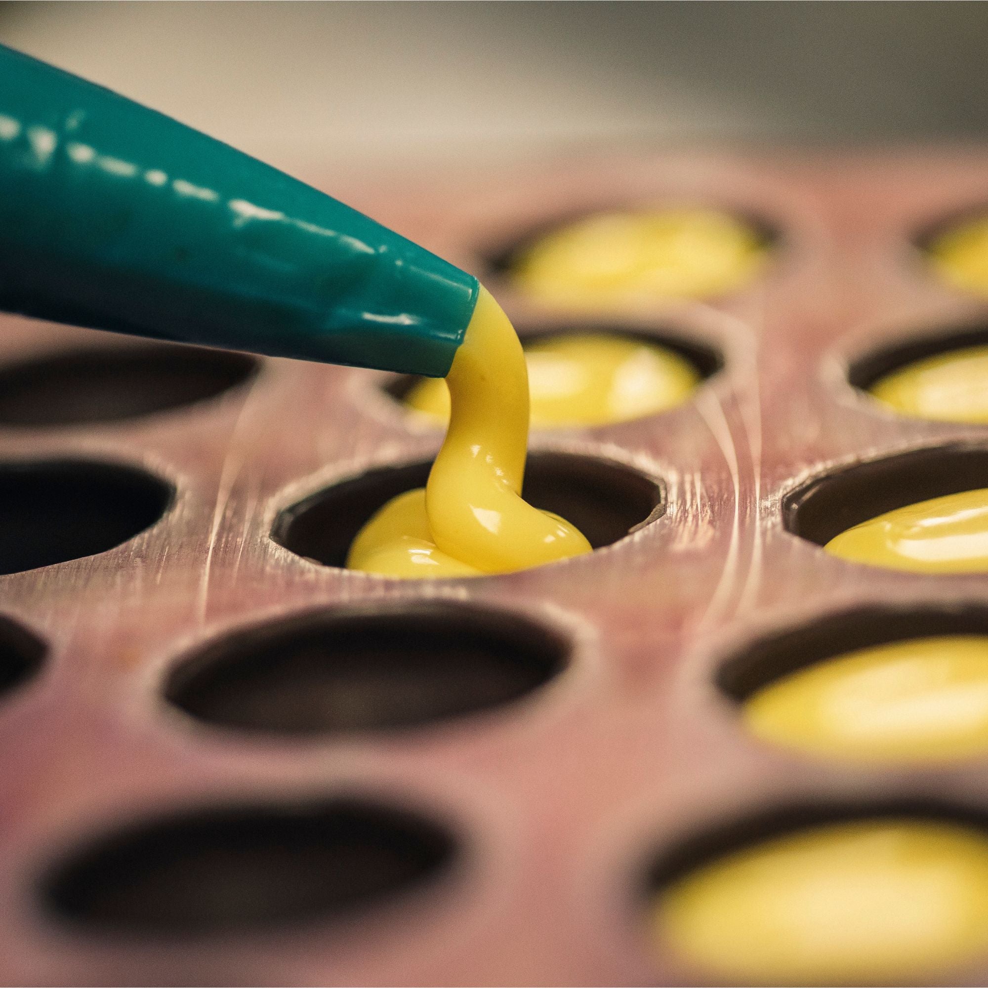 Yellow ganache being poured into a chocolate mould with a piping bag