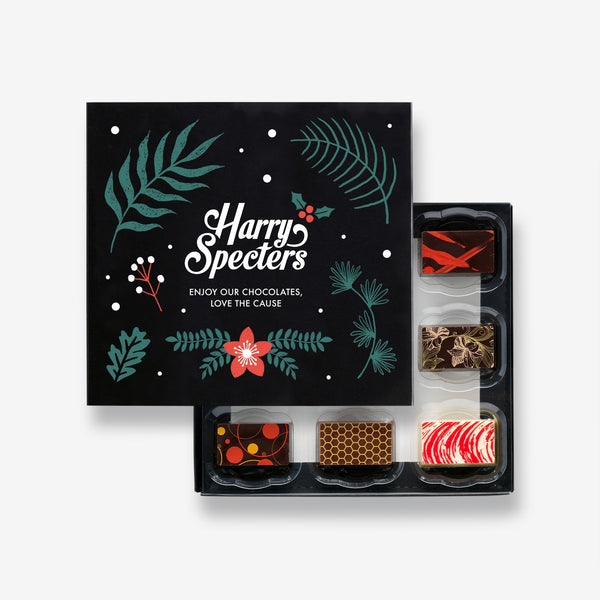 A box of 9 artisan chocolates by Harry Specters including Christmas themed designs partially covered by a festive box lid 