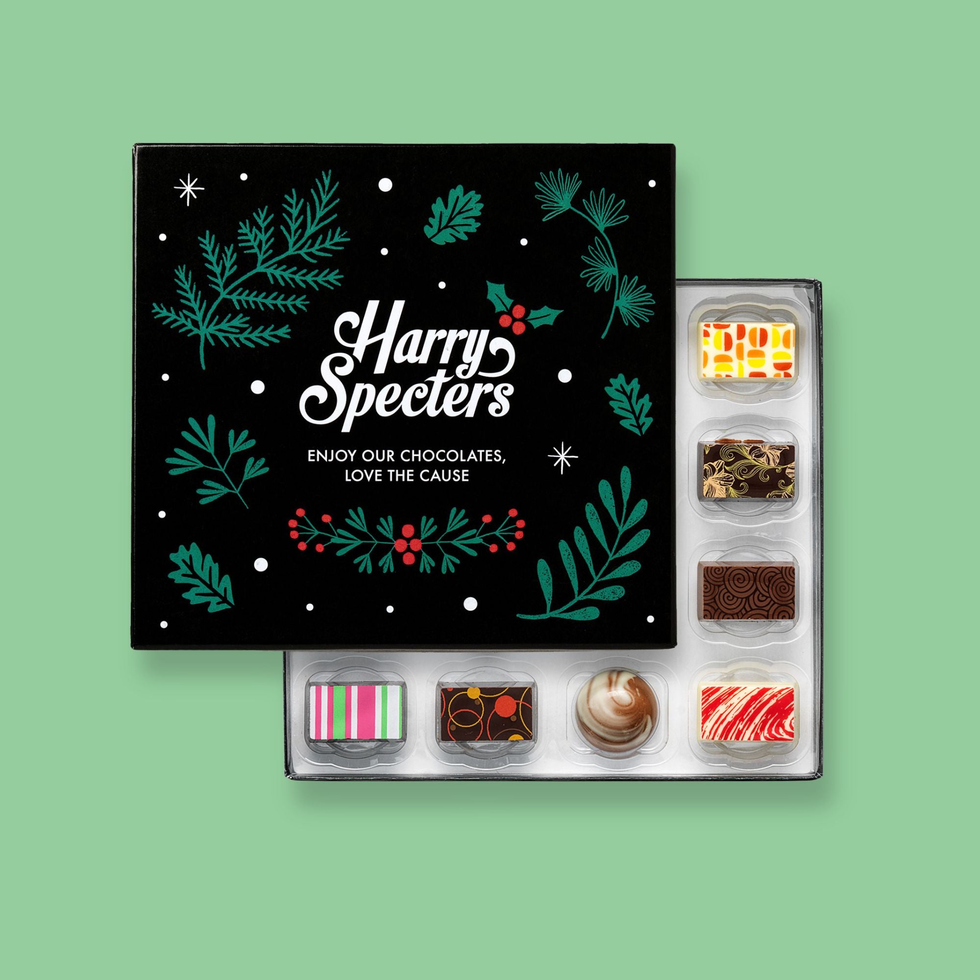 A box of 16 artisan chocolates by Harry Specters including Christmas themed designs partially covered by a festive box lid 