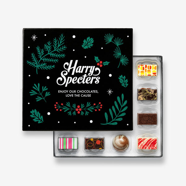 A box of 16 artisan chocolates by Harry Specters including Christmas themed designs partially covered by a festive box lid 