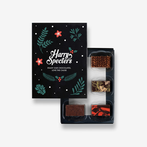 A box of 6 artisan chocolates by Harry Specters including a Christmas themed chocolate partially covered by a box lid 