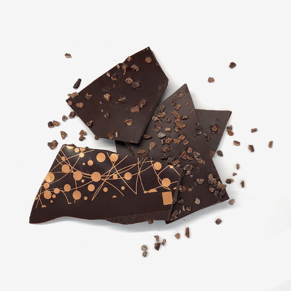 A pile of vegan dark chocolate shards decorated with roasted cocoa nibs