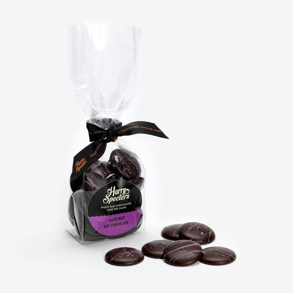A bag of dark hot chocolate melts filled with hazelnut next to a small pile of chocolate buttons 