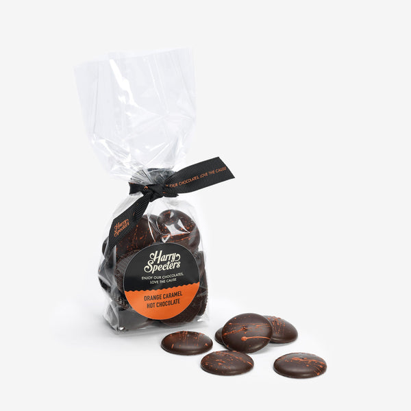 A bag of dark hot chocolate melts filled with orange caramel next to a small pile of chocolate buttons 