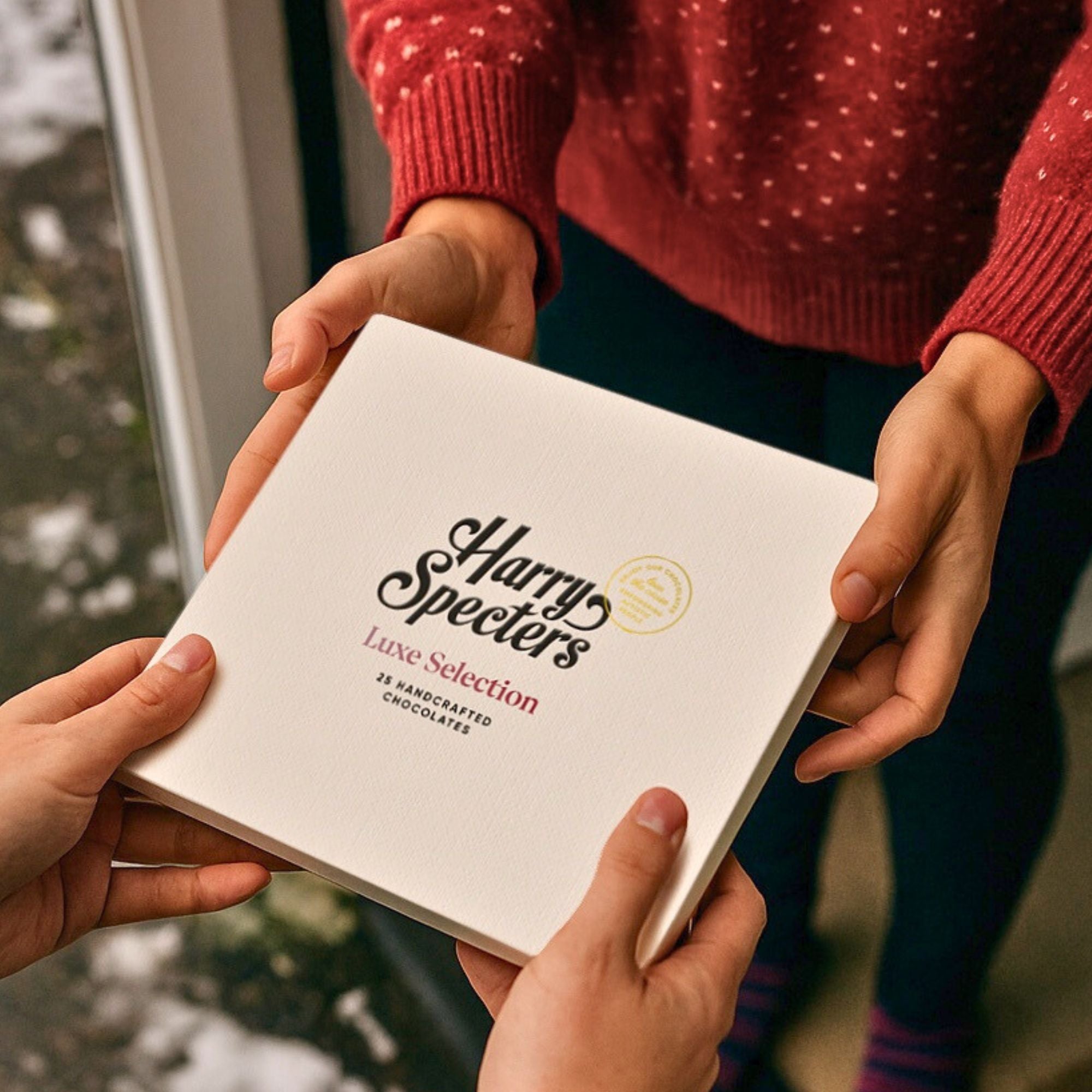 Person holding a 'Harry Specter's Lave Selection' chocolate box with another person's hands.