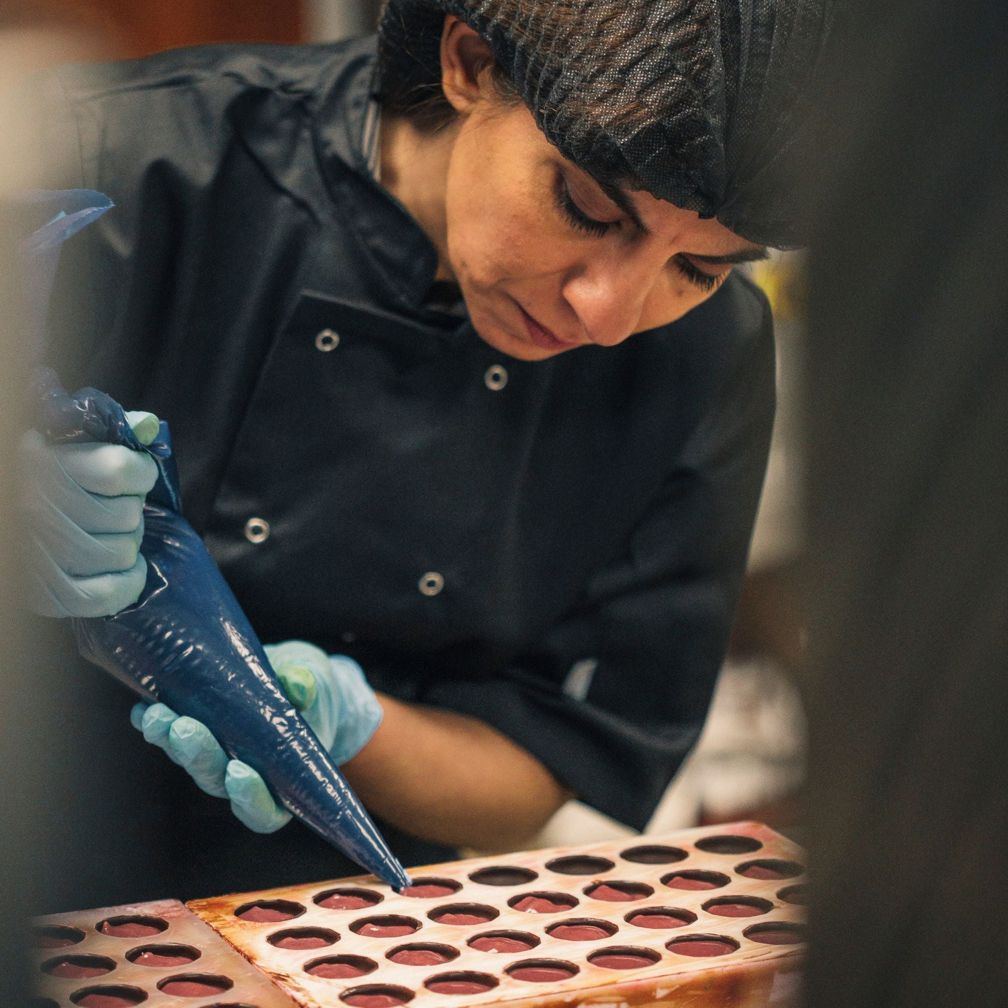 An artisan chocolatier piping filling into chocolate moulds