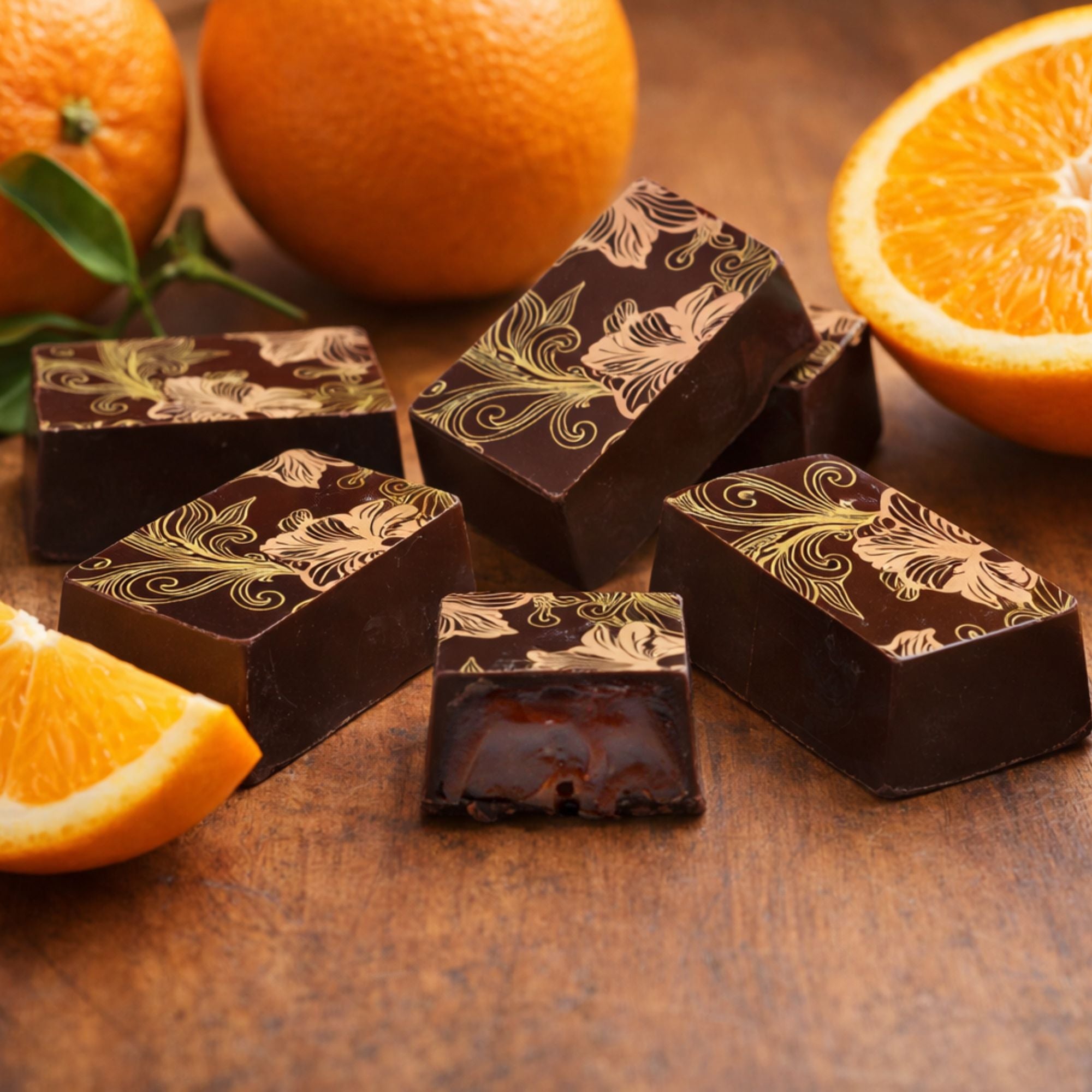 Orange caramel chocolates with decorative patterns on a wooden surface with oranges.