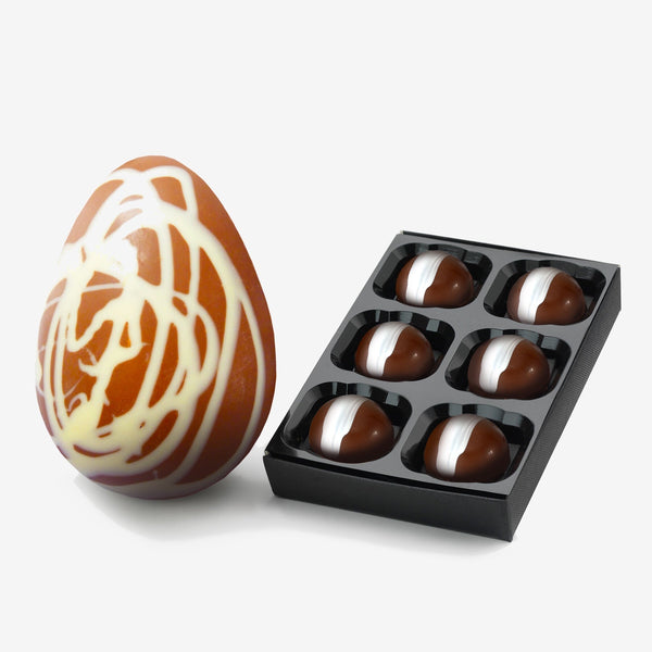 A caramel chocolate Easter egg decorated with a white chocolate swirl next to a box of 6 milk caramel chocolates