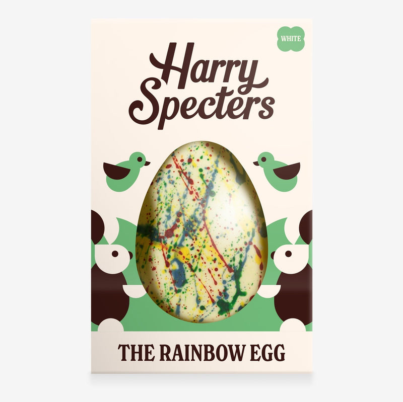 A white chocolate Easter egg decorated with rainbow splatter in a colourful box with an Easter bunny design