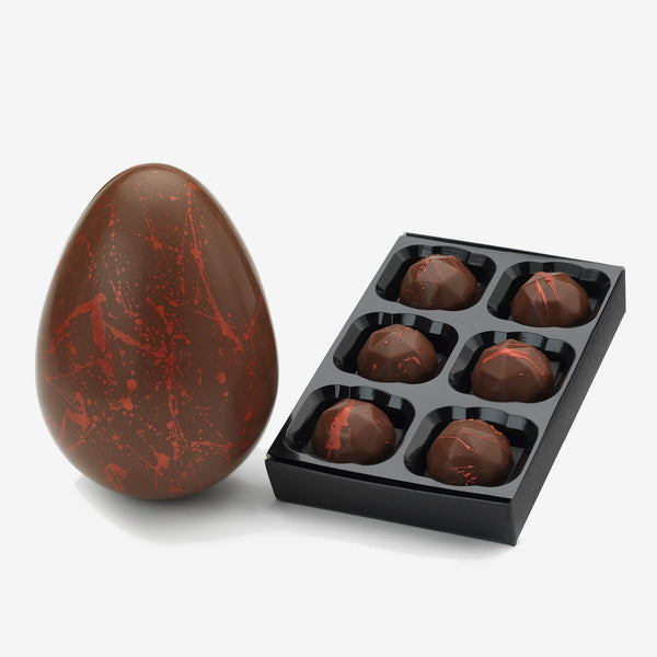 A milk chocolate Easter egg decorated with red splatter next to a box of 6 milk chocolates
