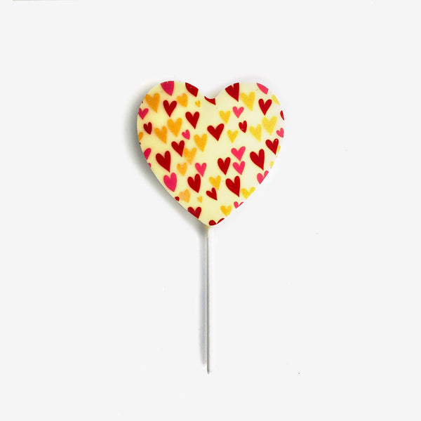 A heart shaped white chocolate lollipop featuring a colourful heart design